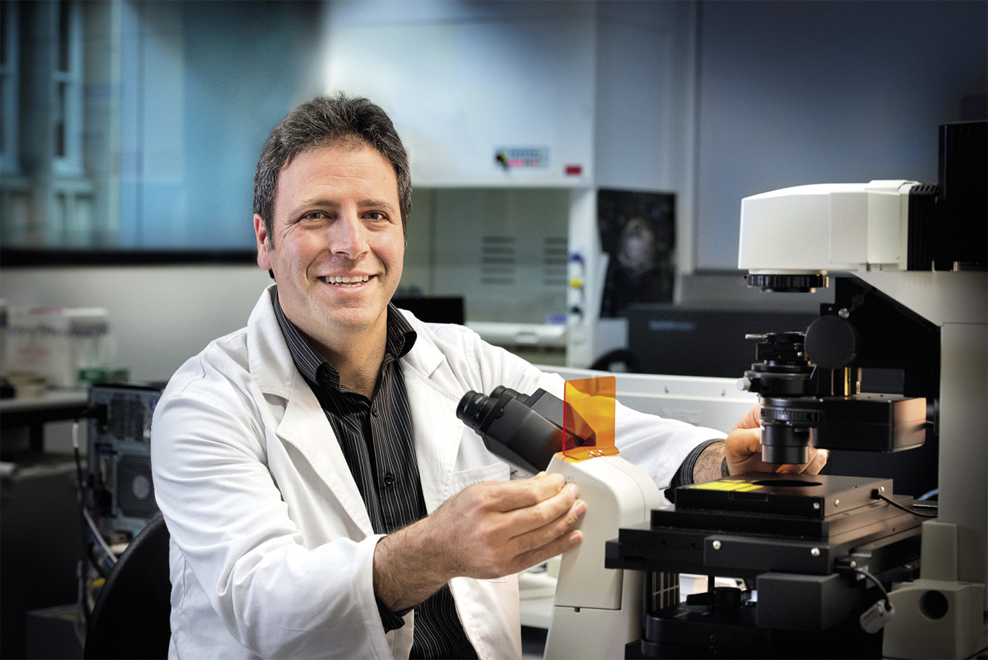 Scientist smiling near a large microscope in a lab coat